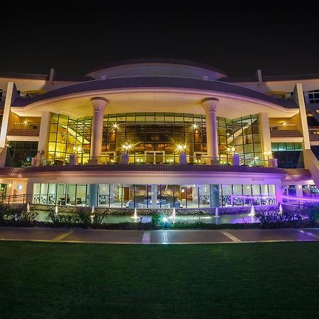 Al Raha Beach Resort & Spa Abu Dhabi Exterior photo The photo shows a modern architectural building illuminated at night. The structure has a large central entrance with multiple glass windows, flanked by symmetrical columns. The exterior features a combination of sleek lines and curves, with lighting
