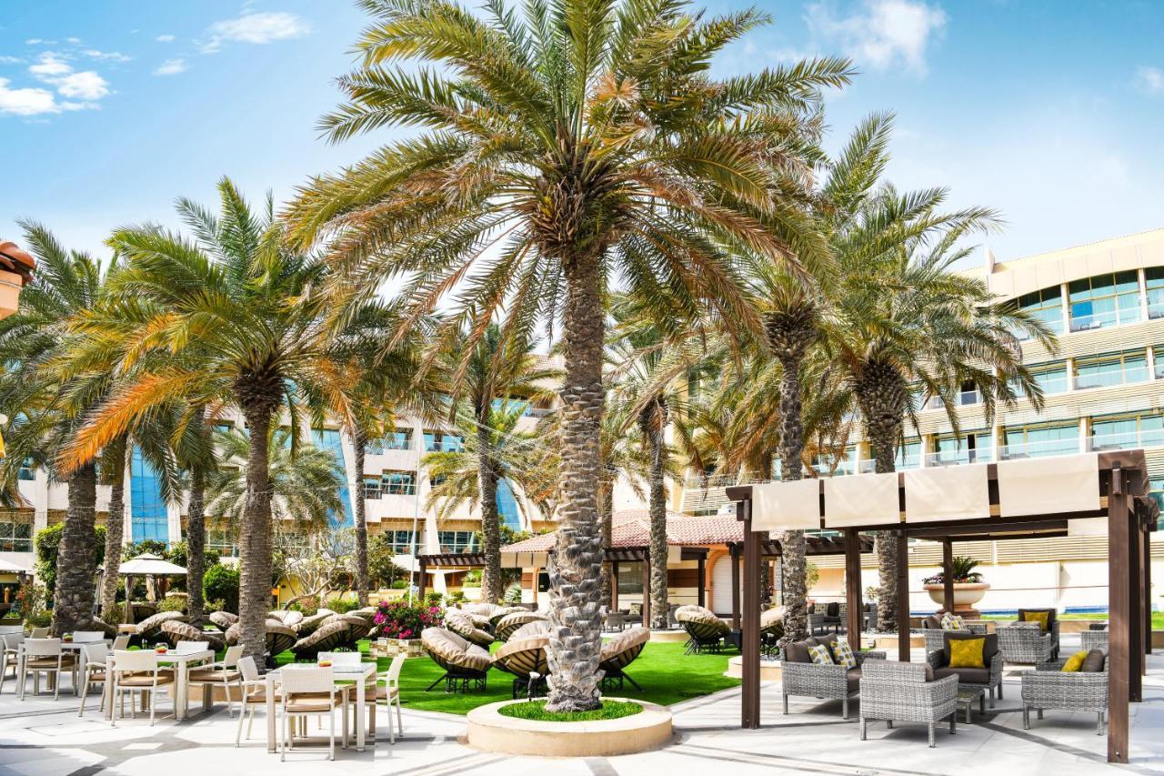 Al Raha Beach Resort & Spa Abu Dhabi Exterior photo The photo shows a picturesque outdoor area, likely at a resort or hotel. It features several tall palm trees that provide a tropical feel. In the foreground, there are several lounge chairs and seating arrangements, suggesting a relaxing environment.