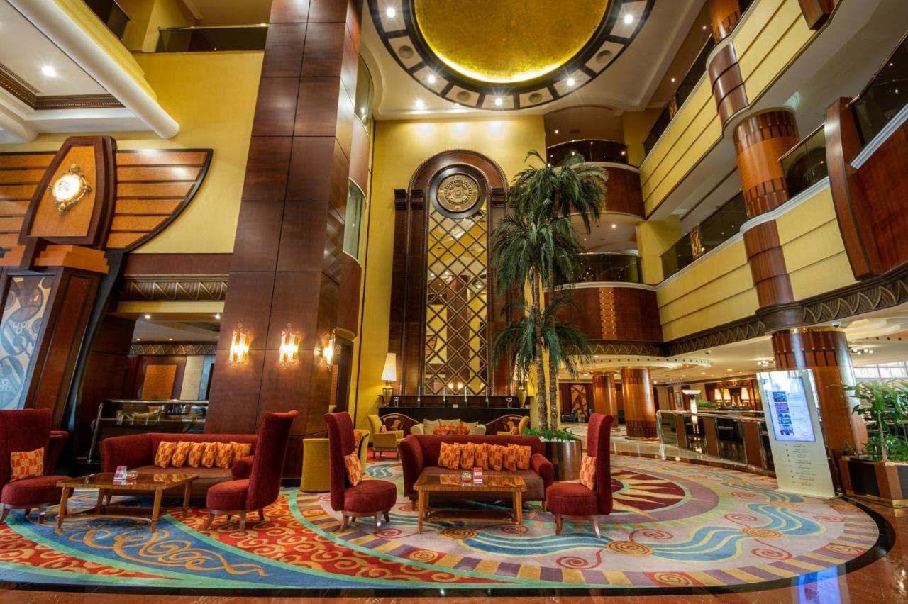 Al Raha Beach Resort & Spa Abu Dhabi Exterior photo The photo shows an elegant lobby interior of a hotel. The space features tall ceilings with decorative lighting and large windows, allowing for natural light. There are several plush seating arrangements, including red armchairs and wooden tables, cr