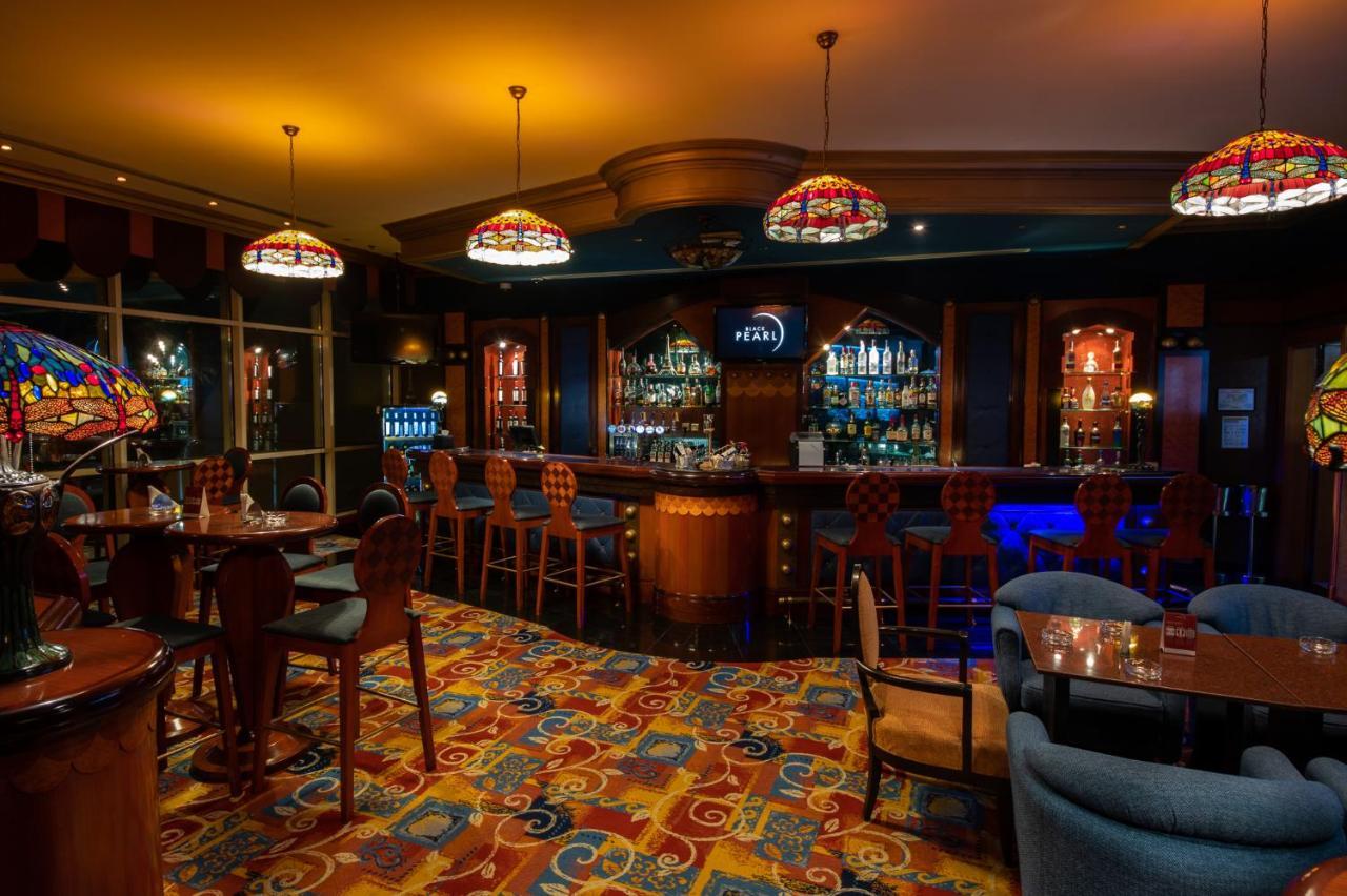 Al Raha Beach Resort & Spa Abu Dhabi Exterior photo The photo shows a cozy bar interior, featuring a well-stocked bar area with various bottles displayed on shelves. The bar is illuminated by colorful stained glass light fixtures, creating a warm and inviting atmosphere. The floor is covered with a vi