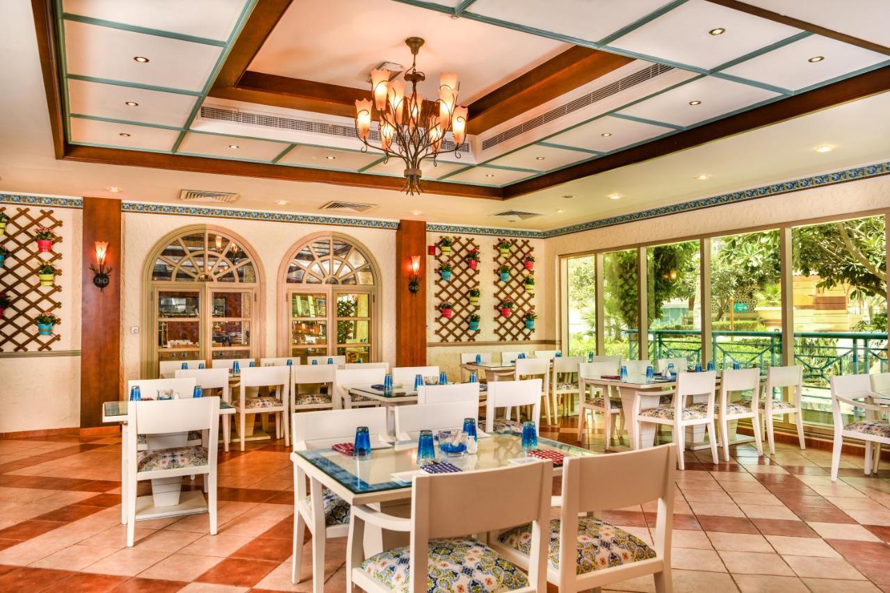 Al Raha Beach Resort & Spa Abu Dhabi Exterior photo The photo shows the interior of a restaurant or dining area. The space has a warm and inviting atmosphere, featuring a mix of decorative elements. 

- **Seating**: There are several white wooden tables and chairs arranged throughout the area, some wi