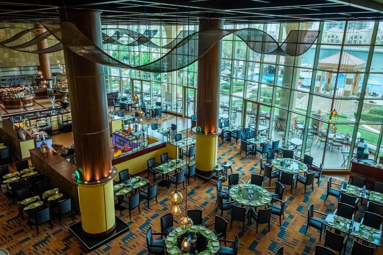 Al Raha Beach Resort & Spa Abu Dhabi Exterior photo The photo shows the interior of a restaurant with a modern design. It features large windows allowing natural light to flood the space, creating an inviting atmosphere. The dining area is furnished with round tables covered with green tablecloths and