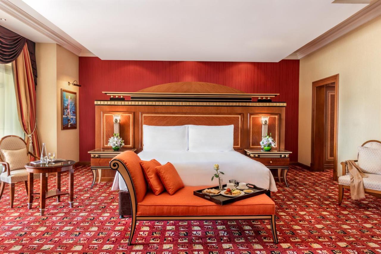 Al Raha Beach Resort & Spa Abu Dhabi Exterior photo The photo shows an elegantly designed hotel room. The room features a large bed with white linens and a decorative headboard. The walls are painted in a warm red color, and there are side tables with lamps beside the bed. 

There is an orange sofa or