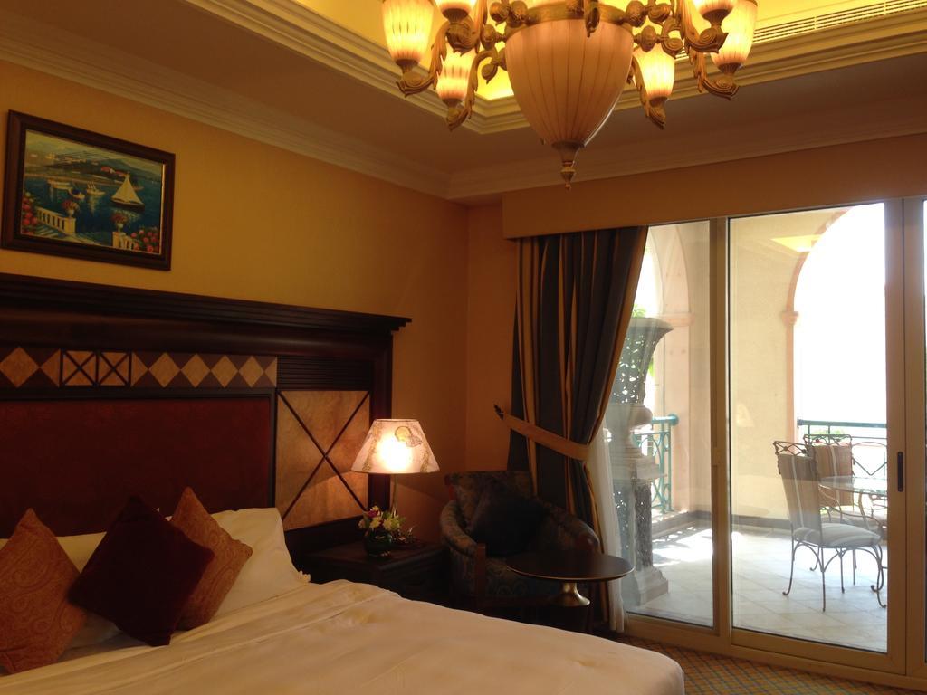 Al Raha Beach Resort & Spa Abu Dhabi Exterior photo The photo shows the interior of a hotel room. The room features a large bed with decorative cushions and a wooden headboard. There's a bedside lamp emitting a warm light, and a painting is hung on the wall above the bed. To the right, there's a windo