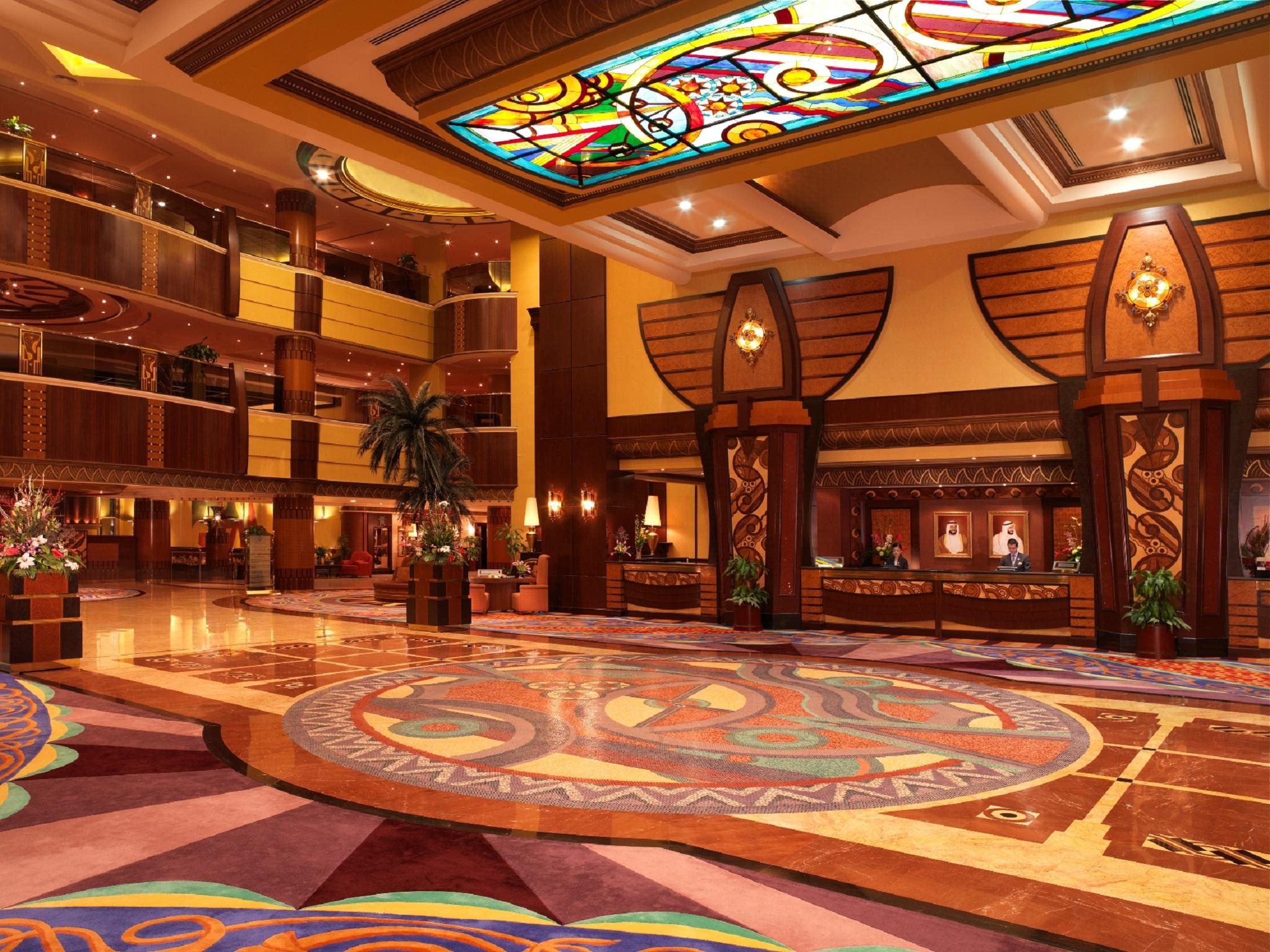 Al Raha Beach Resort & Spa Abu Dhabi Interior photo The photo depicts an elegantly designed hotel lobby. It features a grand ceiling with intricate stained glass and decorative patterns. The floor is adorned with colorful, ornate designs, including circular patterns. The lobby is spacious, with wooden