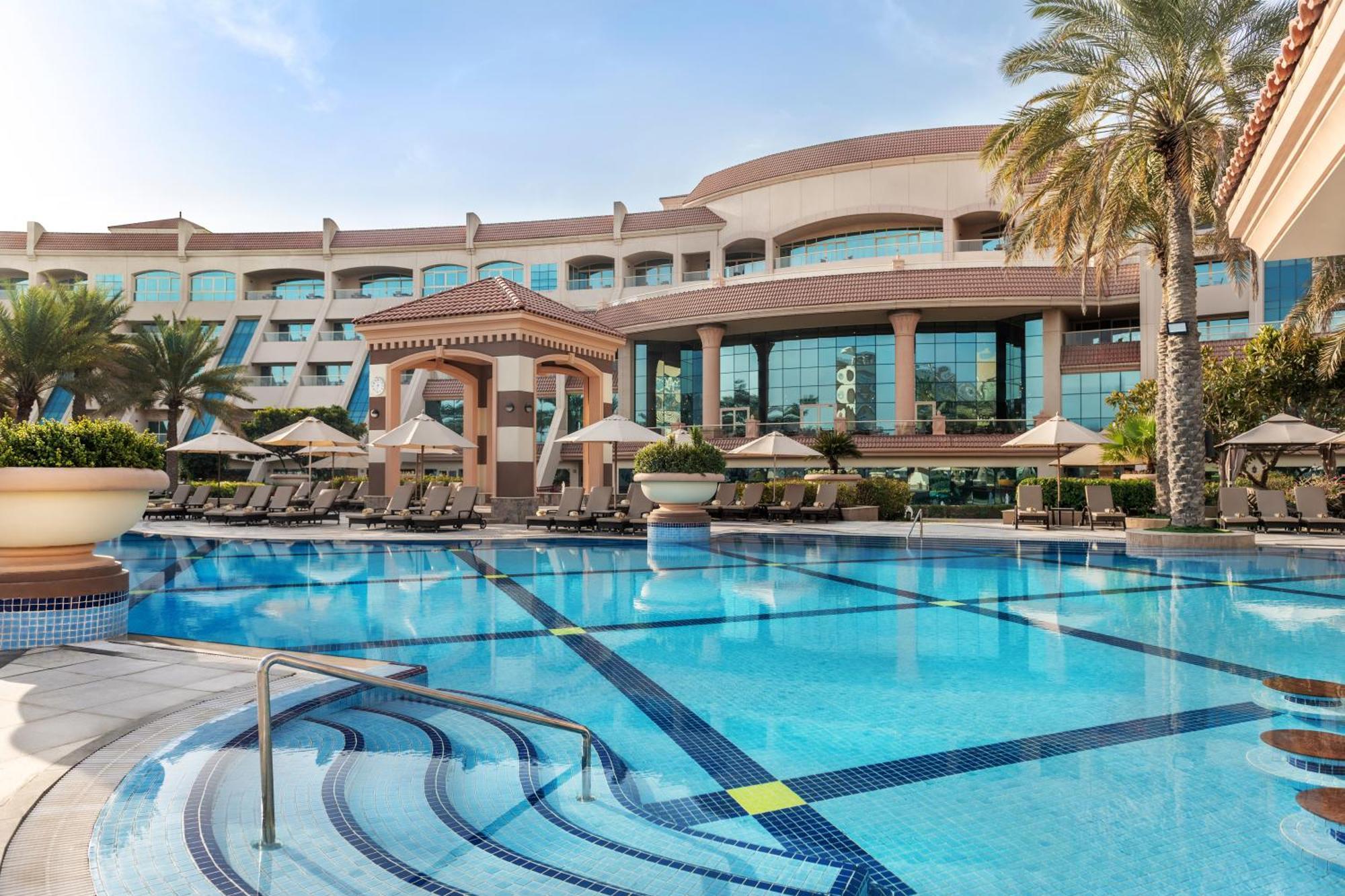 Al Raha Beach Resort & Spa Abu Dhabi Exterior photo The photo shows a luxurious resort with a large swimming pool in the foreground. The pool has a clean, blue surface and features lounge chairs on the surrounding deck. In the background, there is a stylish and modern hotel building with multiple stor
