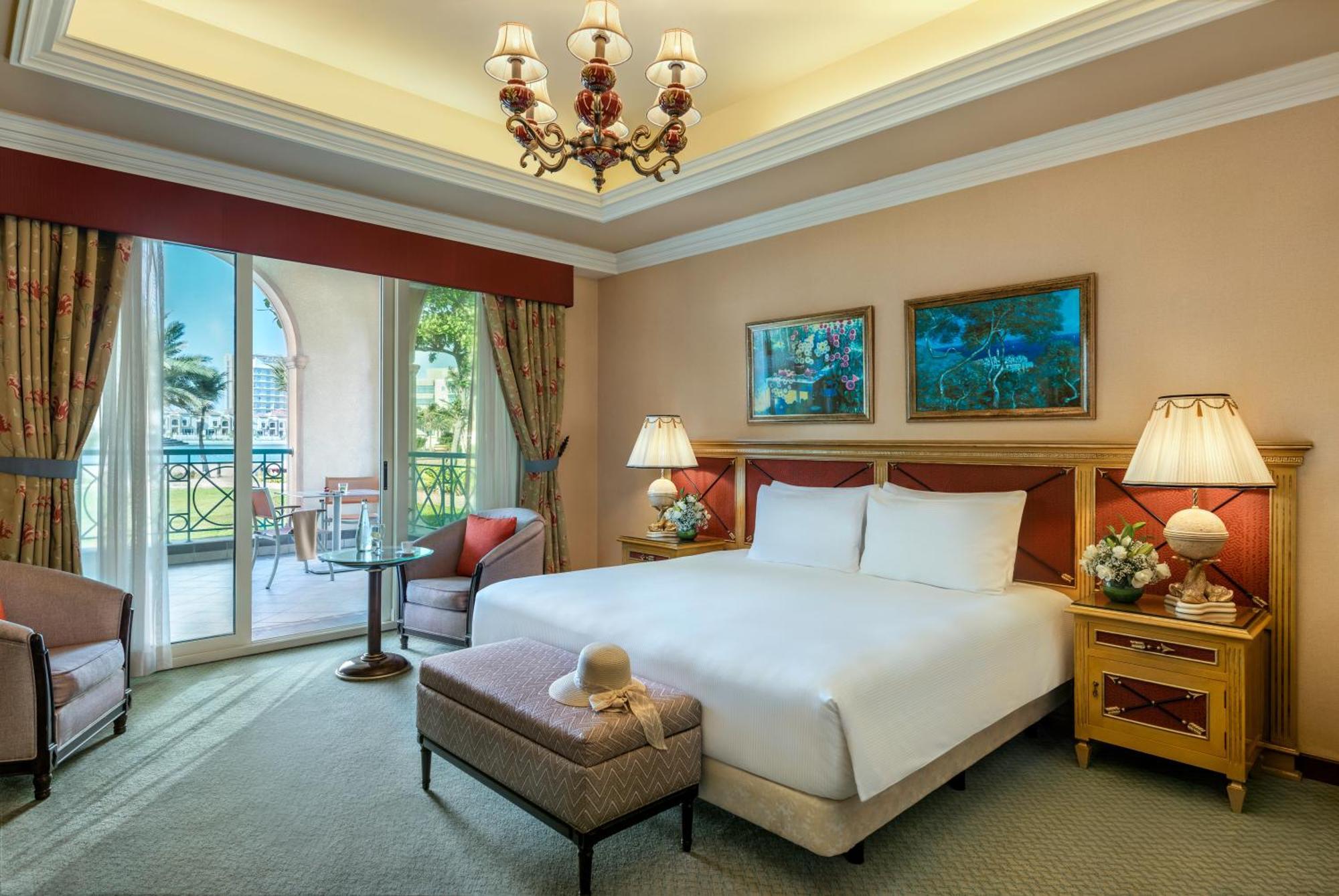 Al Raha Beach Resort & Spa Abu Dhabi Exterior photo The image depicts a well-furnished hotel room. It features a large bed with white linens, flanked by two bedside lamps. Above the bed, there are two pieces of artwork hanging on the walls. To the side, there is a comfortable armchair and a small tabl