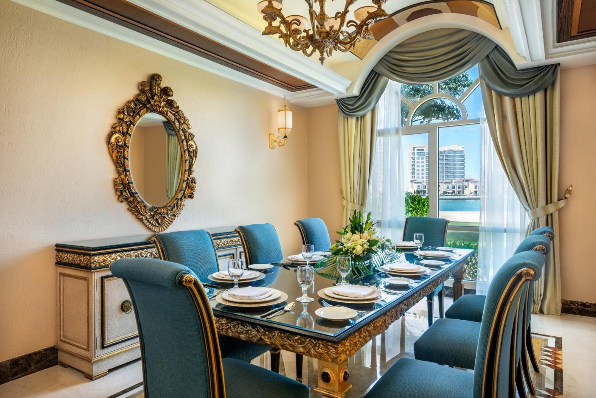 Al Raha Beach Resort & Spa Abu Dhabi Exterior photo The photo features an elegantly decorated dining room. It includes a long, polished table set for a meal with plates, glasses, and decorative items, surrounded by plush blue chairs. The room is adorned with sophisticated details, such as an ornate mi