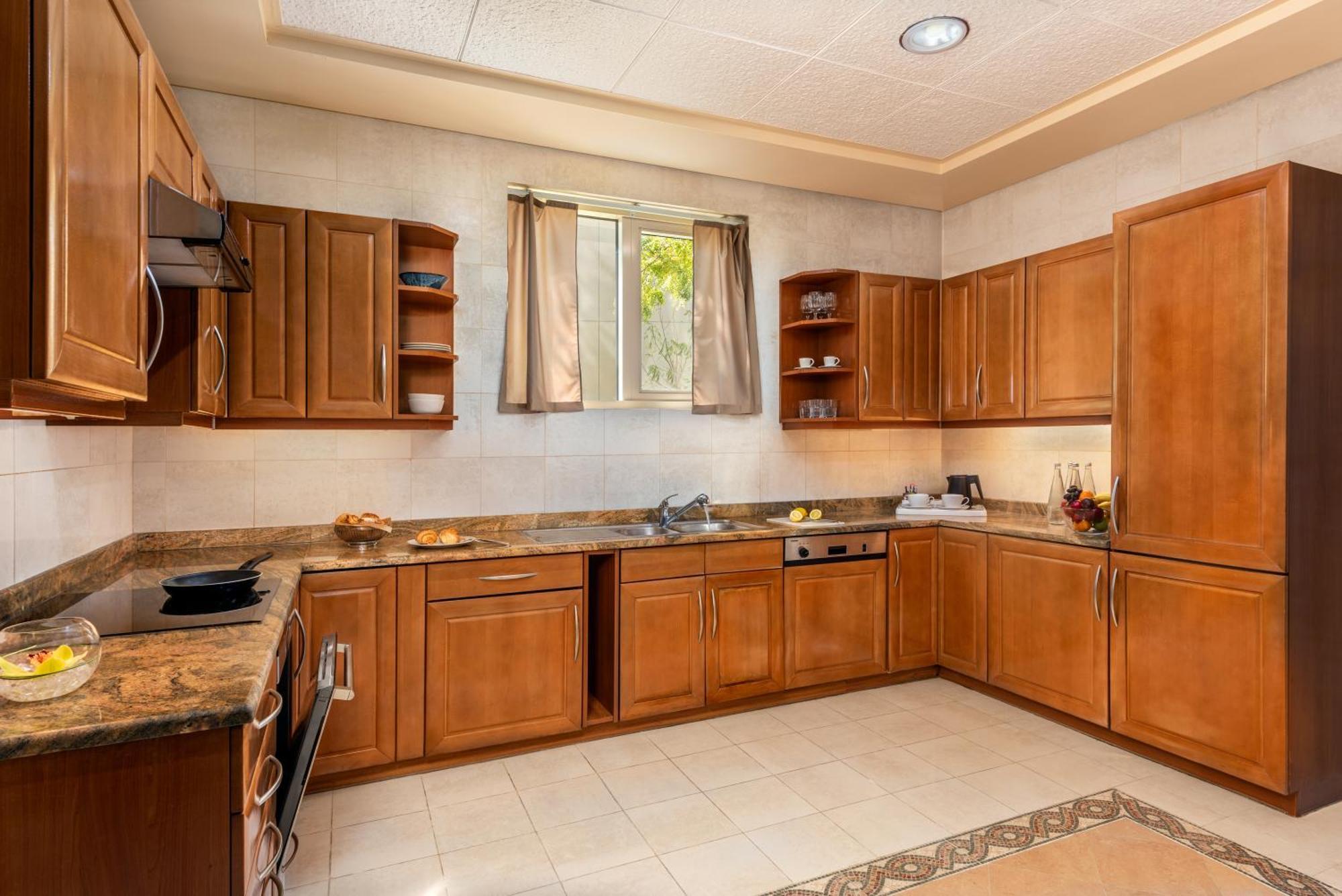 Al Raha Beach Resort & Spa Abu Dhabi Exterior photo The photo shows a cozy kitchen featuring wooden cabinets with a rich brown finish, providing a warm and inviting atmosphere. The countertops are made of a light-colored stone, complementing the cabinetry. There is a window above the sink, allowing na