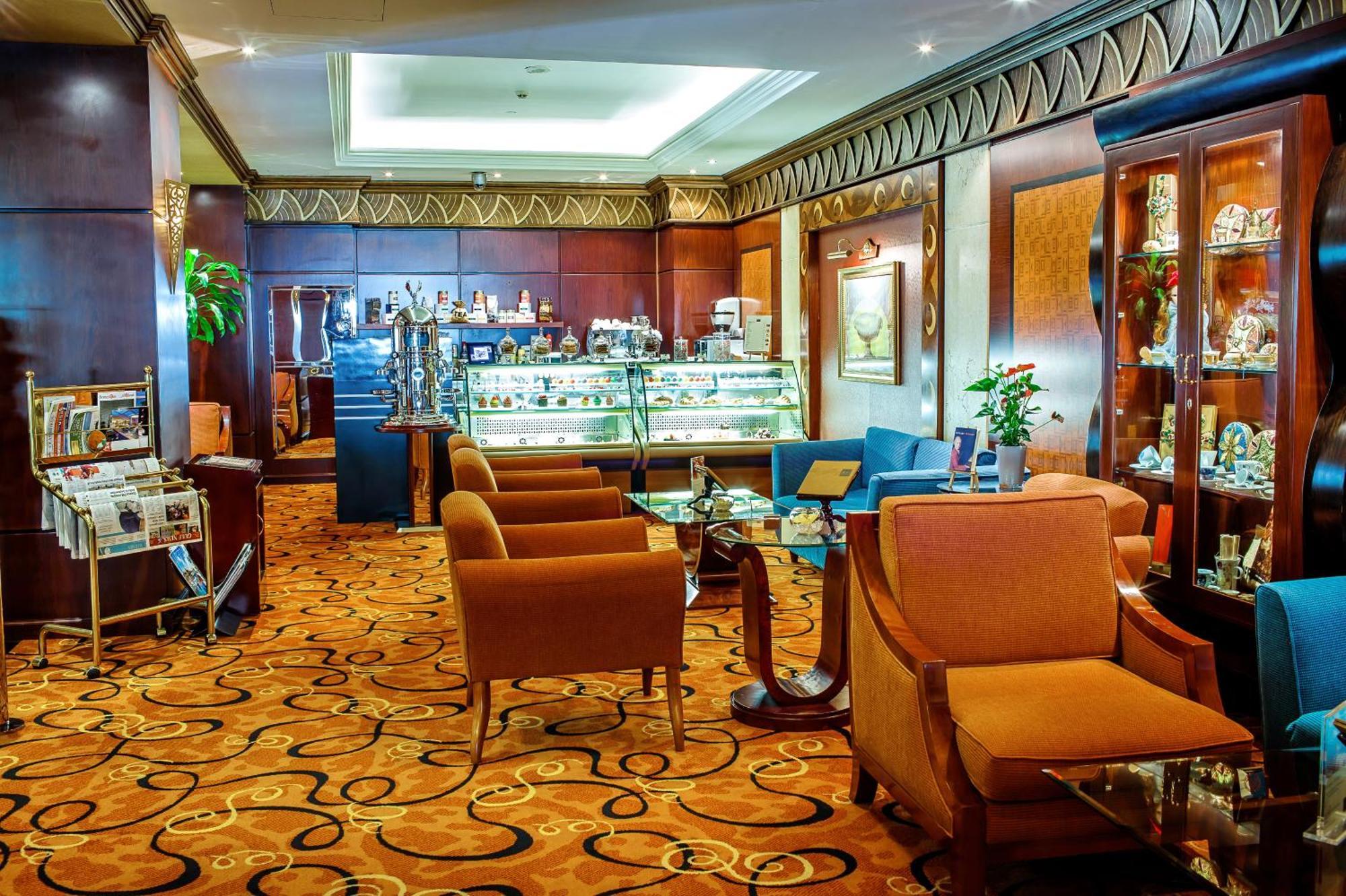Al Raha Beach Resort & Spa Abu Dhabi Exterior photo The photo shows a cozy and elegantly designed lounge or café area. It features plush seating with brown armchairs and a blue couch. In the background, there is a display case filled with various items, likely including pastries or decorative goods. T