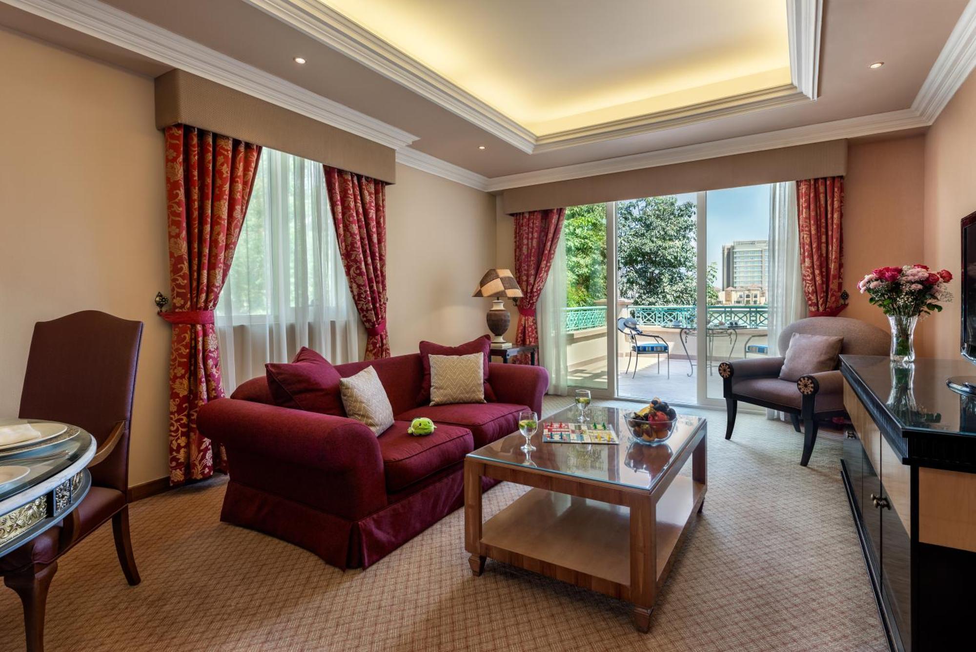 Al Raha Beach Resort & Spa Abu Dhabi Exterior photo The photo shows a well-decorated hotel room or living area. It features a cozy seating arrangement with a deep red couch adorned with cushions, paired with a single chair. There is a glass coffee table in front of the couch, which is set on a plush c