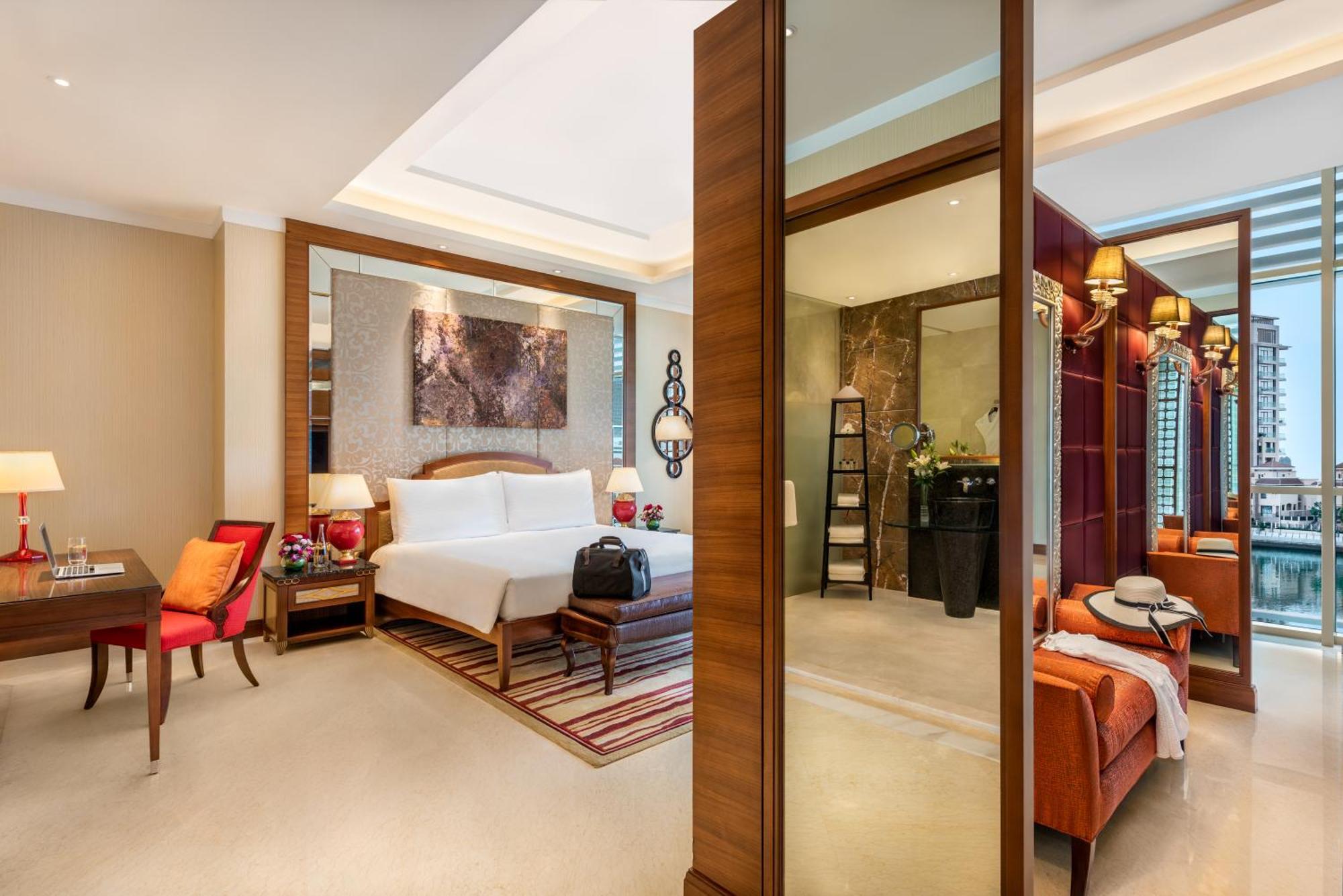 Al Raha Beach Resort & Spa Abu Dhabi Exterior photo The photo shows a luxurious hotel room with a modern design. The room features a large bed with white linens, flanked by bedside tables with lamps. There is a area with a chair and a small table on the left side, and a vibrant artwork hanging above t