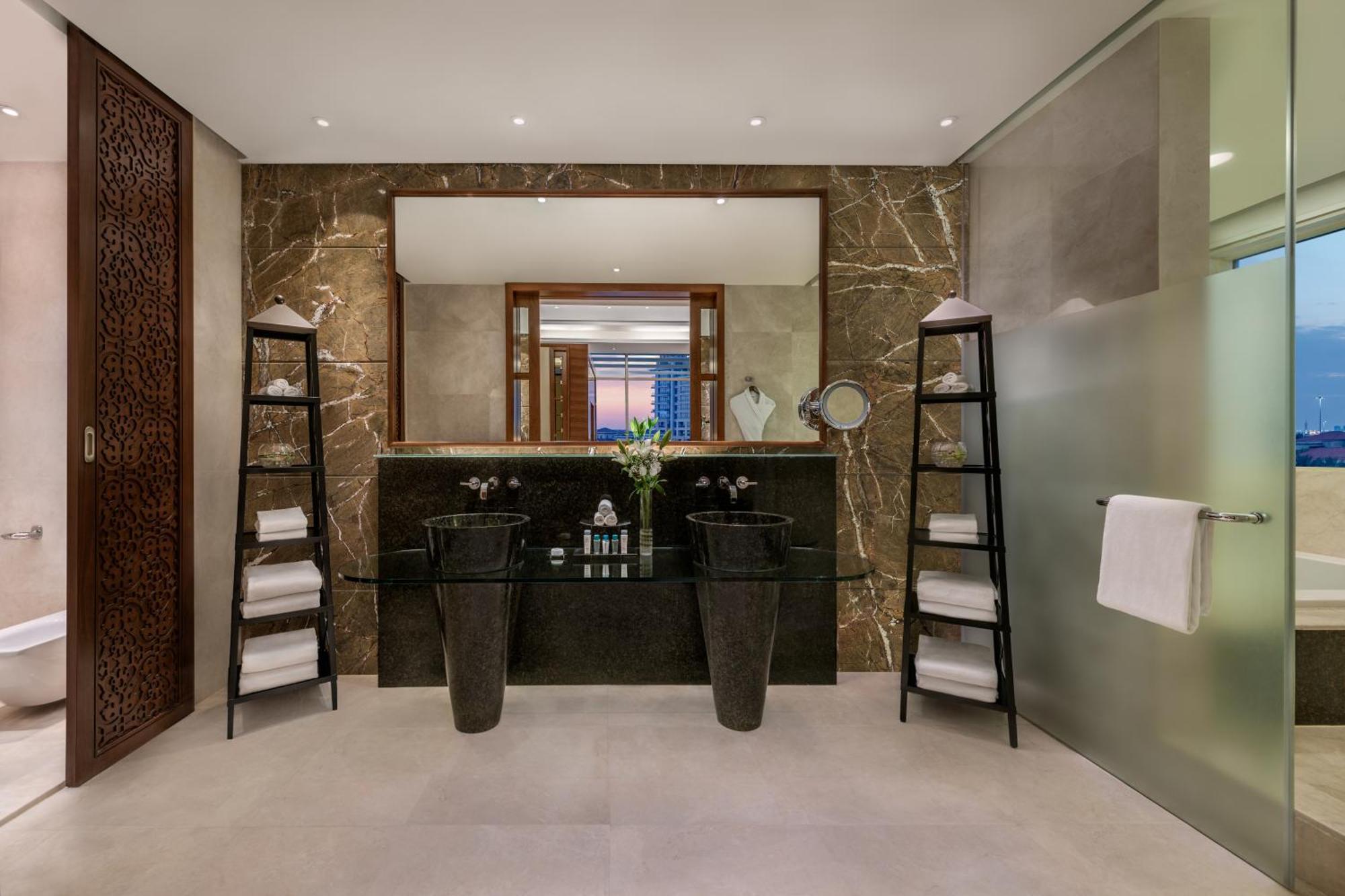Al Raha Beach Resort & Spa Abu Dhabi Exterior photo The photo shows a modern, elegant bathroom interior. It features a large mirror hanging above a double-sink vanity with a dark stone countertop. On either side of the vanity are tall, slender vases that might be holding decorative elements. There are