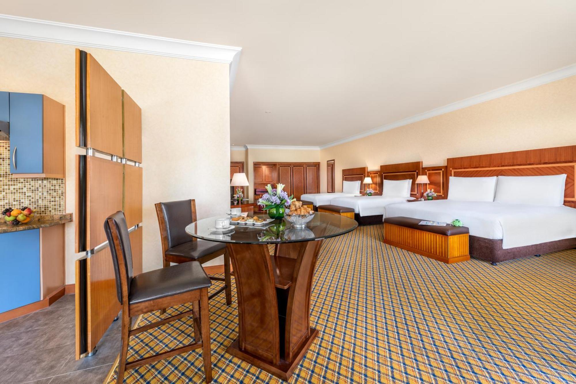 Al Raha Beach Resort & Spa Abu Dhabi Room photo The photo displays a spacious hotel room. It features two large beds with white bedding, a circular glass dining table with a decorative floral centerpiece, and a couple of chairs around it. There is a wooden cabinet along one wall, and the room has 