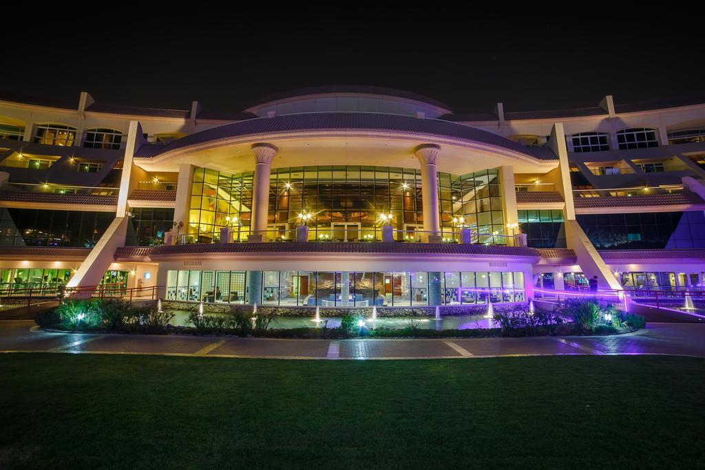 Al Raha Beach Resort & Spa Abu Dhabi Exterior photo The photo shows a modern architectural building illuminated at night. The structure has a large central entrance with multiple glass windows, flanked by symmetrical columns. The exterior features a combination of sleek lines and curves, with lighting